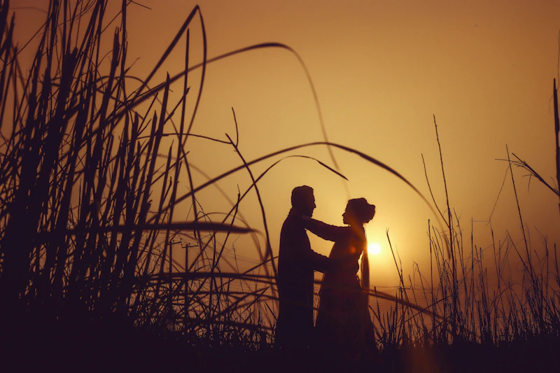 silhouette of man and woman standing on grass field during sunset