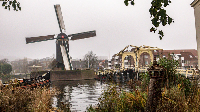 a windmill sitting on top of a river next to tall buildings